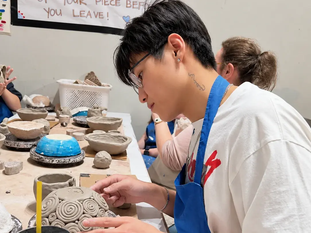 A participant handbuilding pottery at a clay-covered studio table