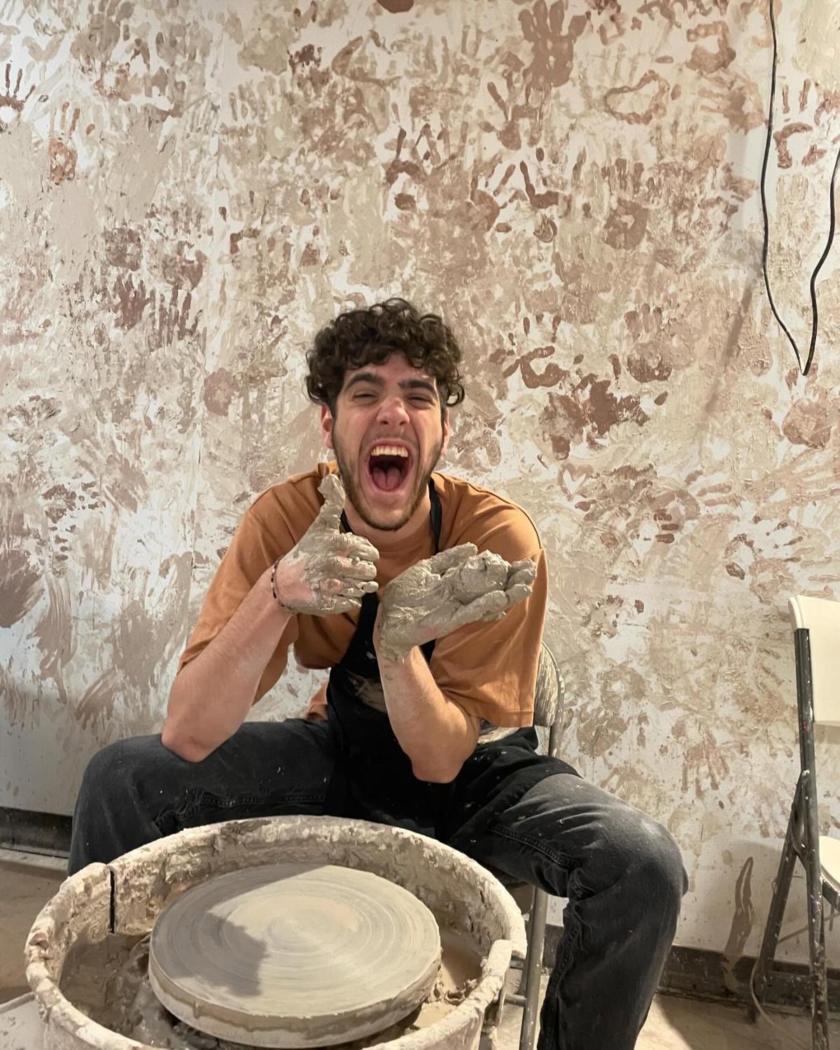 An excited workshop guest giving a clay-covered thumbs-up at a pottery wheel