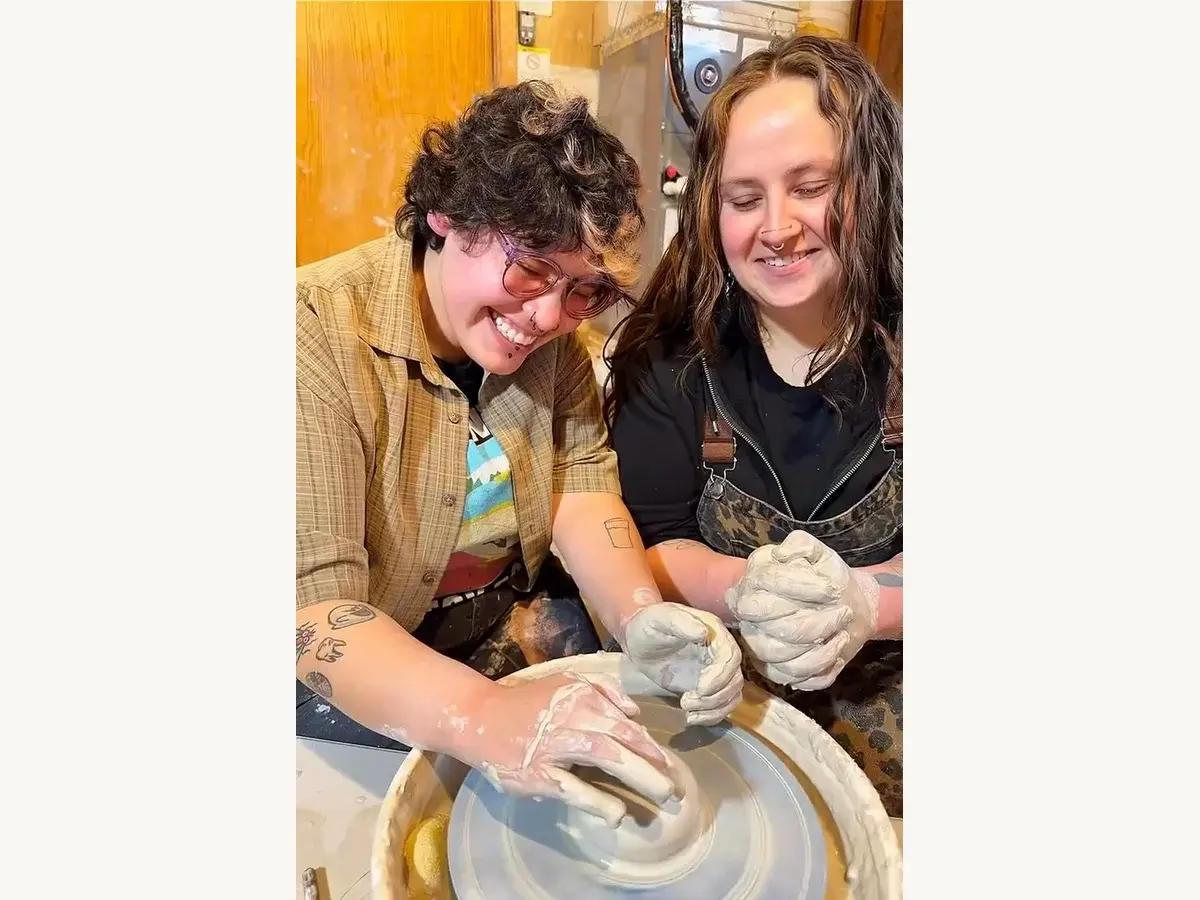 Two guests shaping clay together at a pottery wheel